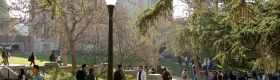 People walk through Bruin Walk on UCLA's campus as the sun is shining. Kerckhoff Hall is in the background.