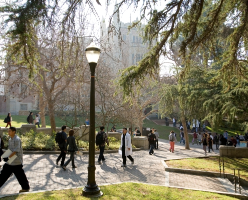 People walk through Bruin Walk on UCLA's campus as the sun is shining. Kerckhoff Hall is in the background.