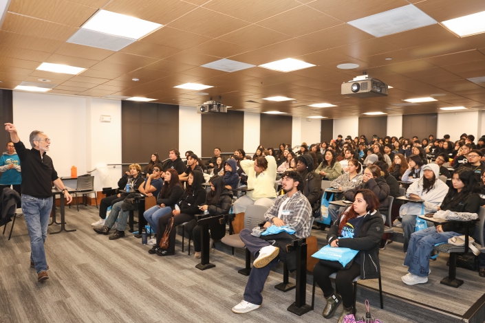 Students seated in a lecture hall while a professor lectures at the front of the room.