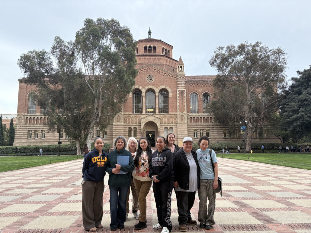 A group of students stand in front of a brick building at UCLA's campus.