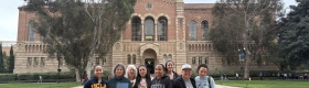 A group of students stand in front of a brick building at UCLA's campus.