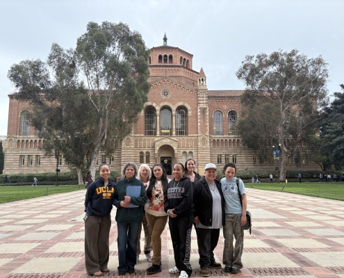 A group of students stand in front of a brick building at UCLA's campus.