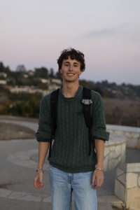 A photo of a young man with brown hair wearing a green shirt and backpack.
