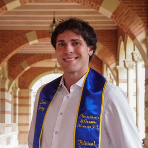 A man with short brown hair wears a white button down and his UCLA graduation sash. The sash says his name, 