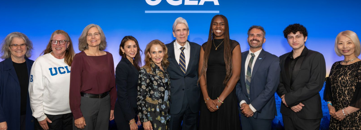 A group of people, including Dean and Vice Provost Adriana Galván and UCLA Chancellor Julio Frenk, stand in front of a blue background that says ONE UCLA.