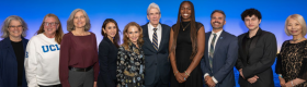 A group of people, including Dean and Vice Provost Adriana Galván and UCLA Chancellor Julio Frenk, stand in front of a blue background that says ONE UCLA.