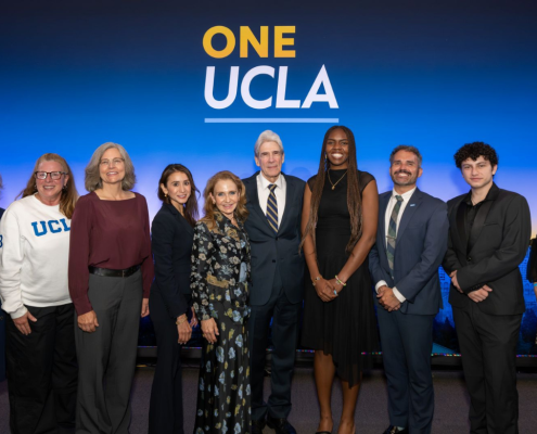 A group of people, including Dean and Vice Provost Adriana Galván and UCLA Chancellor Julio Frenk, stand in front of a blue background that says ONE UCLA.