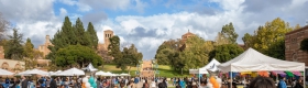 People mingle among balloons and canopy tents on Wilson Plaza at UCLA under a blue but cloudy sky.