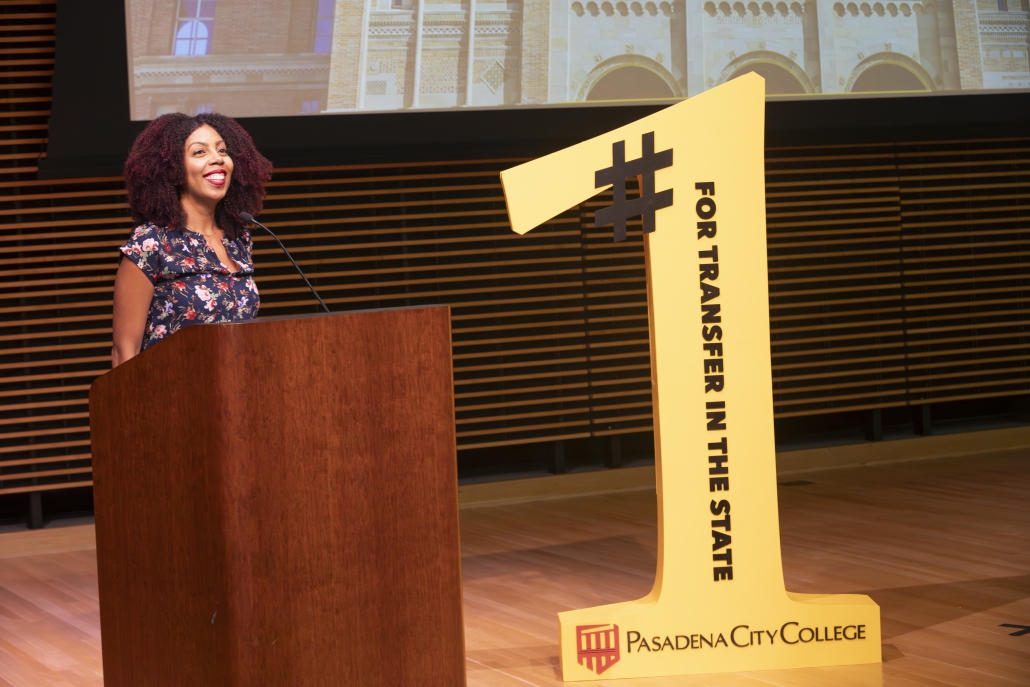 A woman stands at a podium next to a large yellow number one that syas #For Transfer in the State and the Pasadena City College Logo.