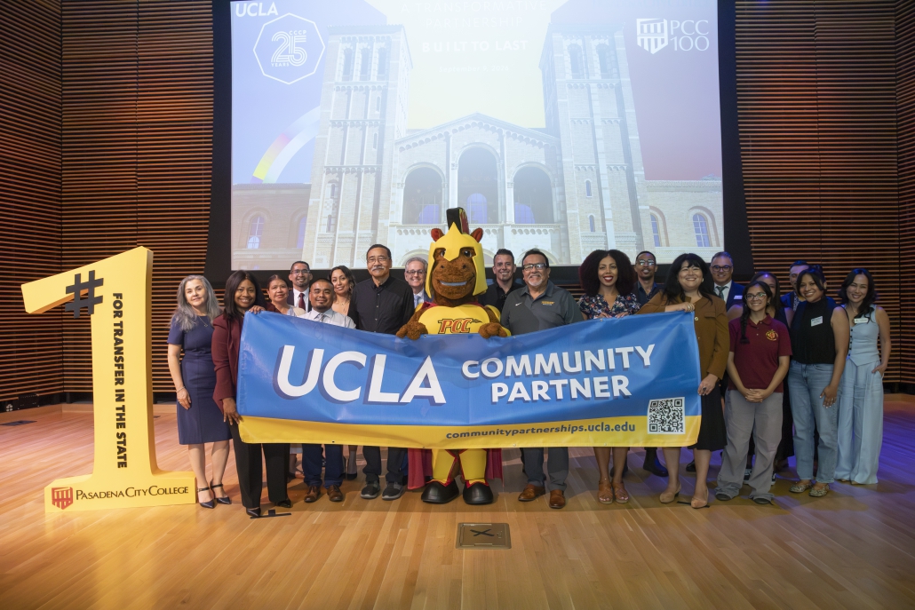 A group of people stands on stage holding a blue banner that reads "UCLA COMMUNITY PARTNER". A mascot stands in the center, and a large yellow cutout on the left reads "#1 FOR TRANSFER IN THE STATE / PASADENA CITY COLLEGE". A presentation screen behind them shows Royce Hall at UCLA along with UCLA and PCC logos.