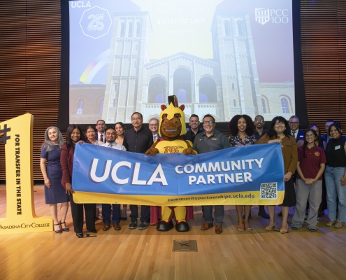 A group of people stands on stage holding a blue banner that reads "UCLA COMMUNITY PARTNER". A mascot stands in the center, and a large yellow cutout on the left reads "#1 FOR TRANSFER IN THE STATE / PASADENA CITY COLLEGE". A presentation screen behind them shows Royce Hall at UCLA along with UCLA and PCC logos.
