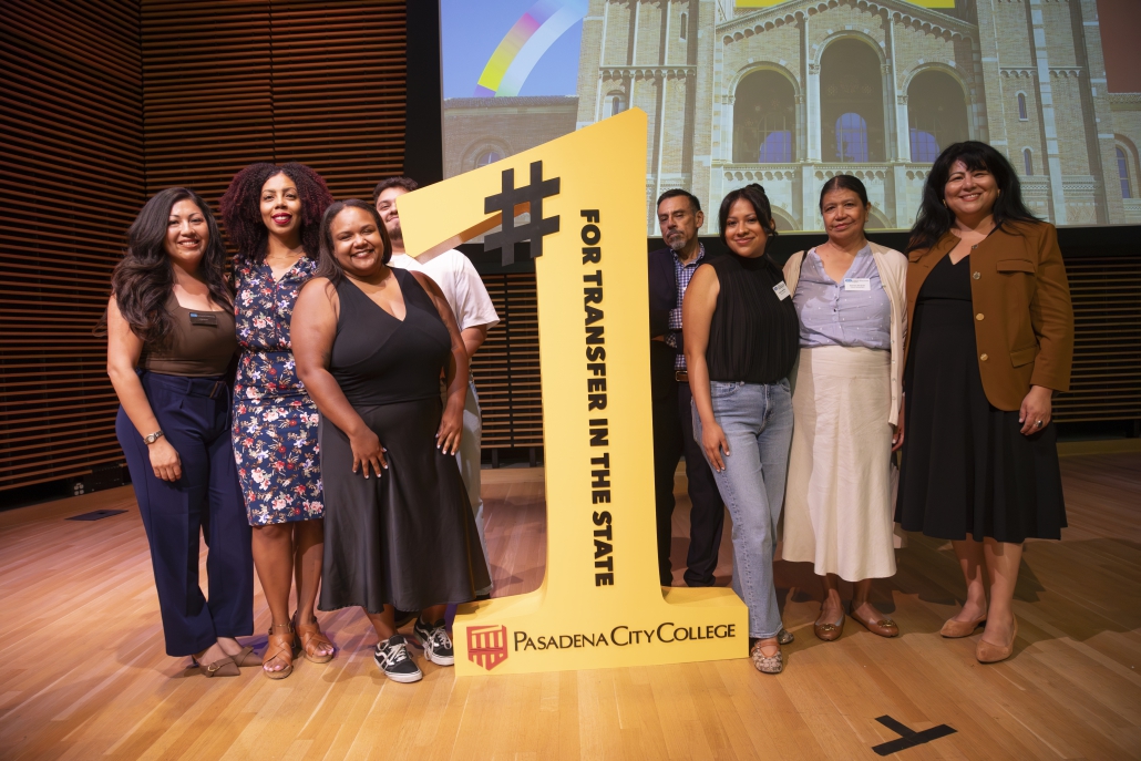 Seven people stand on stage posing on both sides of a large yellow cutout shaped like a number one, which reads "#1 FOR TRANSFER IN THE STATE" above the Pasadena City College logo.